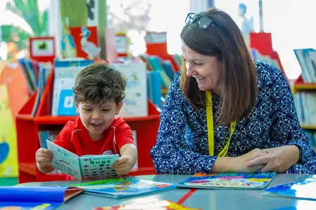 Lower School Boy in the library reading to Teacher with a big smile