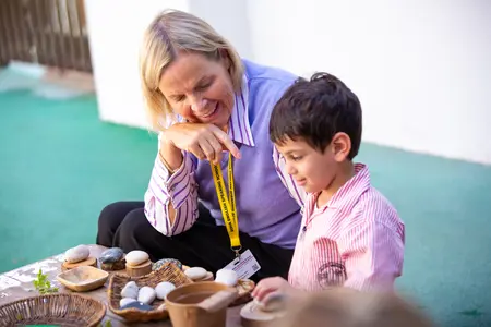 Boy playing with stones in the DESS Lower School garden being helped by the Teacher