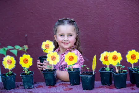 Lower School Girl in the school garden, looking very proud and happy of her growing samplings and gardening achievements 